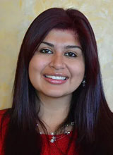 The image is a portrait of a woman with red hair, wearing a dark top and smiling. She has a red-tinged complexion, and her pose suggests a professional or formal setting.
