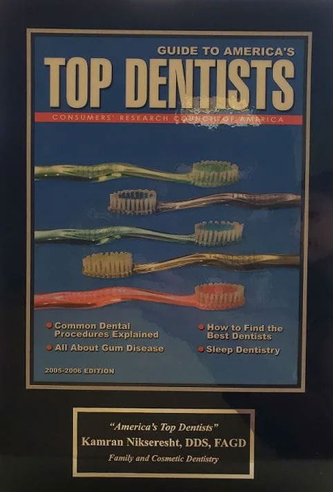 A framed magazine cover with the title 'Top Dentists' displayed prominently, featuring an illustration of multiple toothbrushes in different colors arranged vertically and a text box with information about dental health.