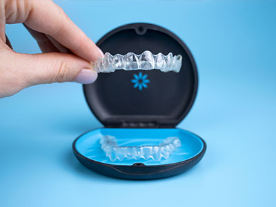 The image shows a hand holding a clear plastic tray containing a set of dental implants, with the box open to reveal the implants inside.
